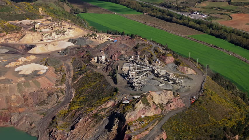 Aerial view of a quarry and mining operation, surrounded by lush green fields and a winding roadway