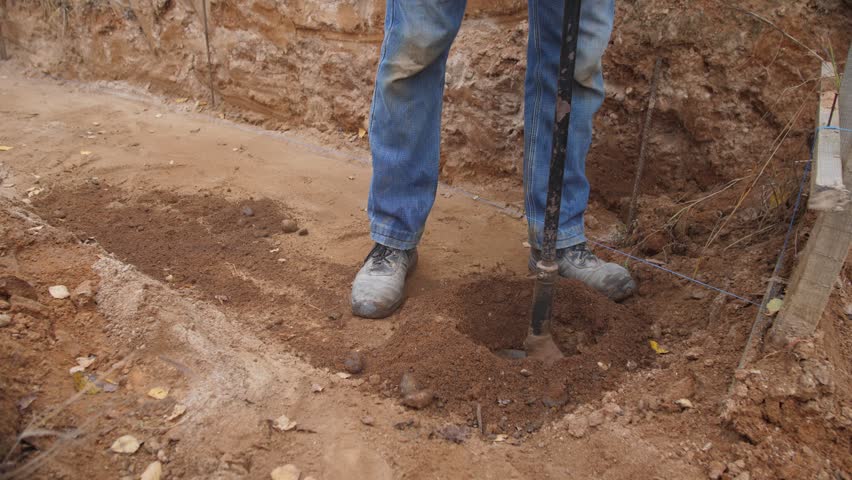foundation crew drilling deep footing with heavy auger, twohanded operation and steady stance, large soil clods ejected into pile, professional construction rhythm and measured spacing