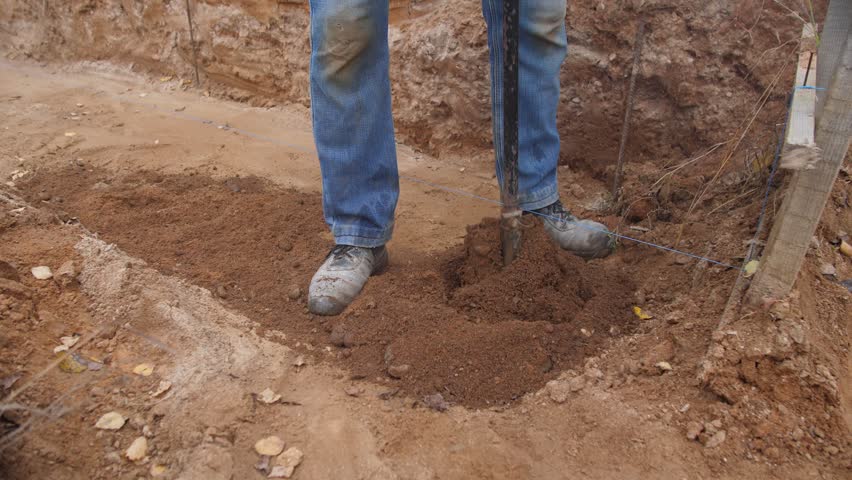 foundation crew drilling deep footing with heavy auger, twohanded operation and steady stance, large soil clods ejected into pile, professional construction rhythm and measured spacing