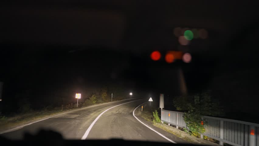 View from a car driving on a dark highway at night, illuminated by headlights. A cinematic, moody atmosphere evoking mystery, solitude, and the calm of night travel.
