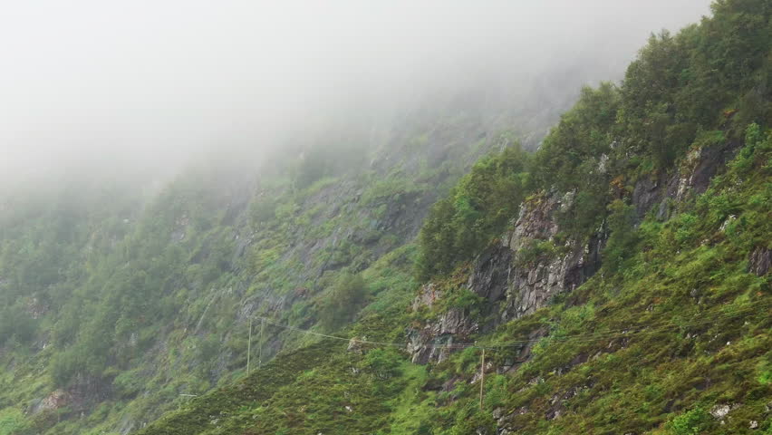 Misty mountainside landscape in Norway showcasing lush greenery and rugged terrain on a foggy day