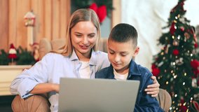 Mother and young boy share happy moments, smiling and waving during a video call on laptop. Festive Christmas decorations create warm. Virtual connection brings happiness and closeness during holidays - Powered by Shutterstock - Get 15% off with code: PIKWIZARD15