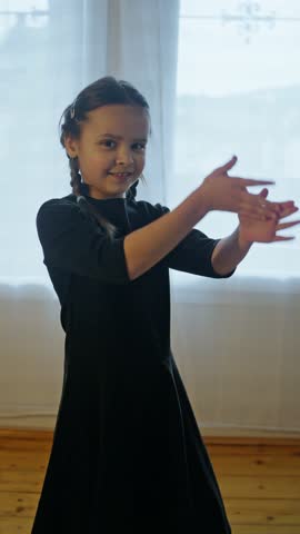 A young girl is gracefully dancing in a stylish black dress, showcasing her joy and lively movement in every step. Slow motion