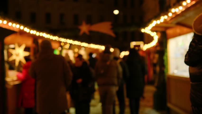 Blurred illuminated Christmas market. People hanging out at Christmas market. Shimmering garlands. Defocused people walking. Winter activities. Beautifully illuminated fair