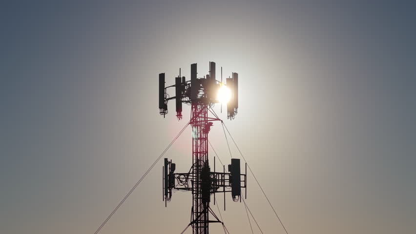 Telecommunication tower with antennas against bright sun and clear blue sky, symbolizing modern wireless communication technology. High quality 4k footage