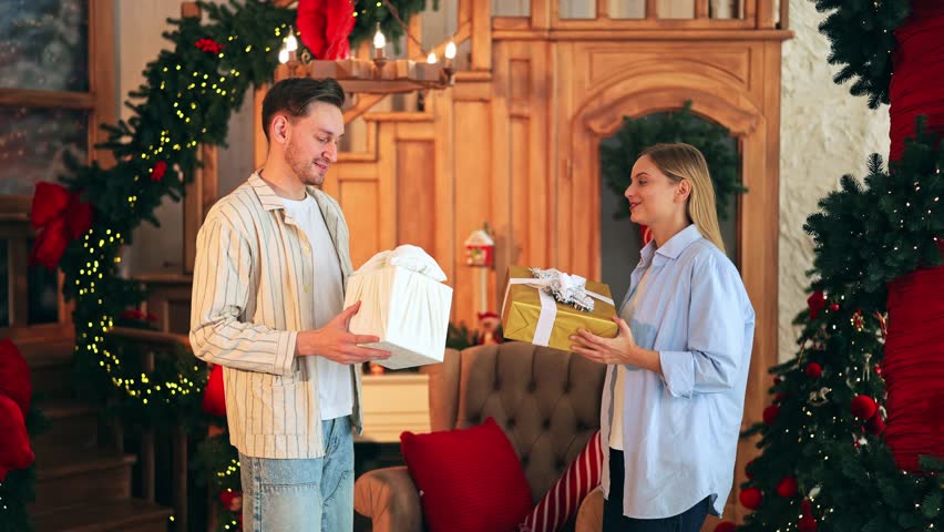 Happy couple joyfully exchanges wrapped presents in beautifully decorated room. Smiles indicate happiness, love, and excitement during festive Christmas season, gifts shared.