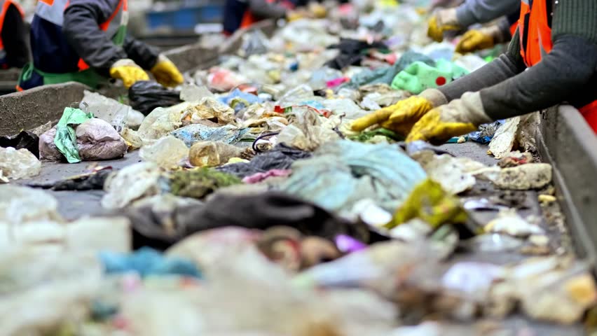 Workers sorting mixed waste by type on a conveyor belt inside a recycling facility. Industrial stage of the waste management and environmental sustainability process.