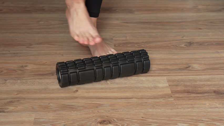 White woman doing foot massage on black roller for training. Rehabilitation exercises. Home workout