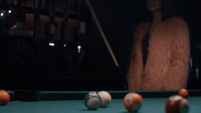 Elegant young woman in a faux fur coat lines up her shot and hits the ball during a friendly pool game in a bar. - Powered by Shutterstock - Get 15% off with code: PIKWIZARD15