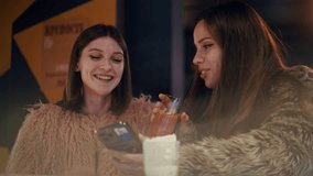 Happy female friends enjoy a night out, using a mobile phone and drinking cocktails at a bar. Russian text says "Fortress" - Powered by Shutterstock - Get 15% off with code: PIKWIZARD15