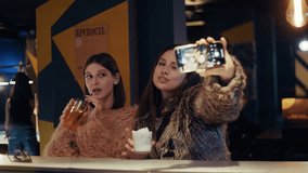 Close-up shot of two young women enjoying cocktails and taking selfies with a smartphone flash at a modern bar in the evening. Russian text says "Fortress" - Powered by Shutterstock - Get 15% off with code: PIKWIZARD15