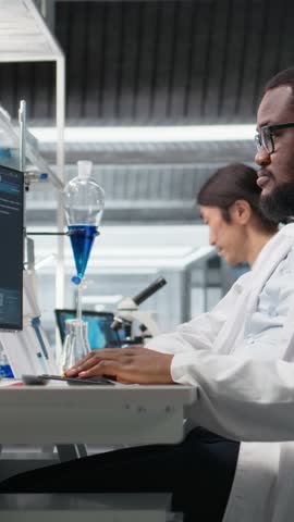 Vertical video Laboratory bioinformatics scientist evaluates genetic markers using PC, analyzing sample properties. Man studies DNA strand mapping and chemical solution components using program on