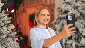 Happy blonde woman takes Christmas selfie video on smartphone. Joyful emotions radiate from smiling face, celebrating holiday season. Communication and digital connection captured video chat online - Powered by Shutterstock - Get 15% off with code: PIKWIZARD15