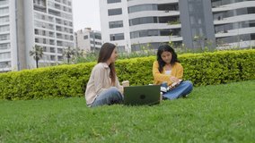 Two young university women sitting on the grass of an urban park. They are studying together using a laptop, books, and drinking coffee - Powered by Shutterstock - Get 15% off with code: PIKWIZARD15