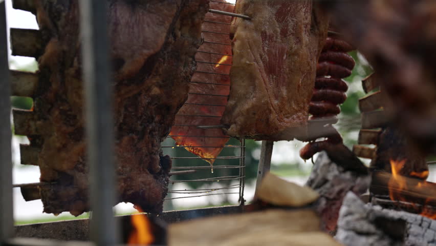 Argentinian meat barbecue cooking over flames in traditional asado with smoke and coals, slow motion detailed cooking