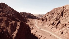 Drone following a car through the red canyons of the Atacama Desert, Chile. Rugged sandstone cliffs, winding dirt road, and bright daylight create a cinematic desert scene - Powered by Shutterstock - Get 15% off with code: PIKWIZARD15