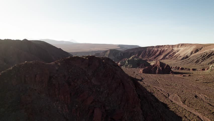 Aerial panorama of Rainbow Valley in the Atacama Desert, Chile. Multicolored hills, rugged terrain, and soft sunlight reveal layers of red, green, and brown minerals in a surreal landscape