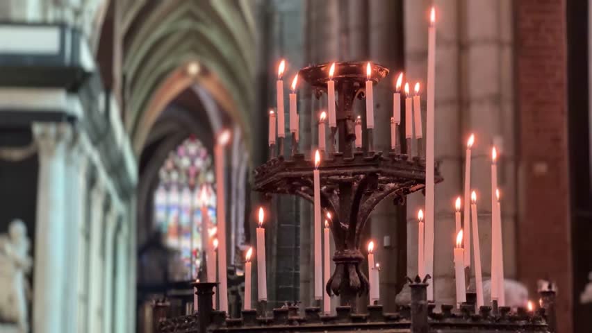 Atmospheric close-up of lit candles inside the historic Saint Bavo Cathedral in Ghent, Belgium, with warm light and Gothic interior details.