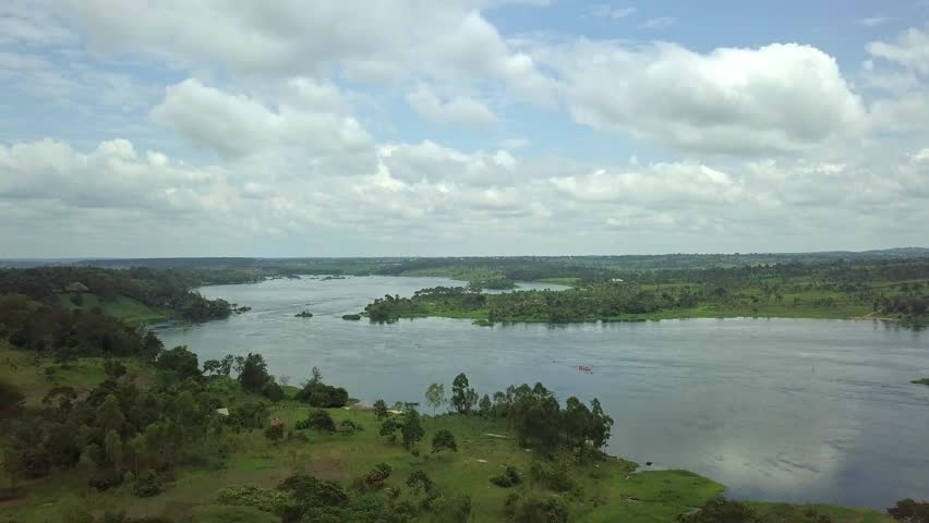 Aerial panorama of the River Nile at Jinja, Uganda, showing wide water channel, forested banks, scattered houses, highlighting the river’s natural beauty and surrounding greenery.