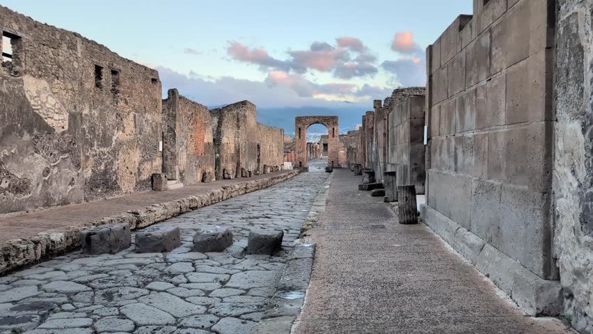 Slow pan left across Pompeii’s ancient stone street at golden hour, showing stepping stones once used to cross flooded roads in the historic Roman city