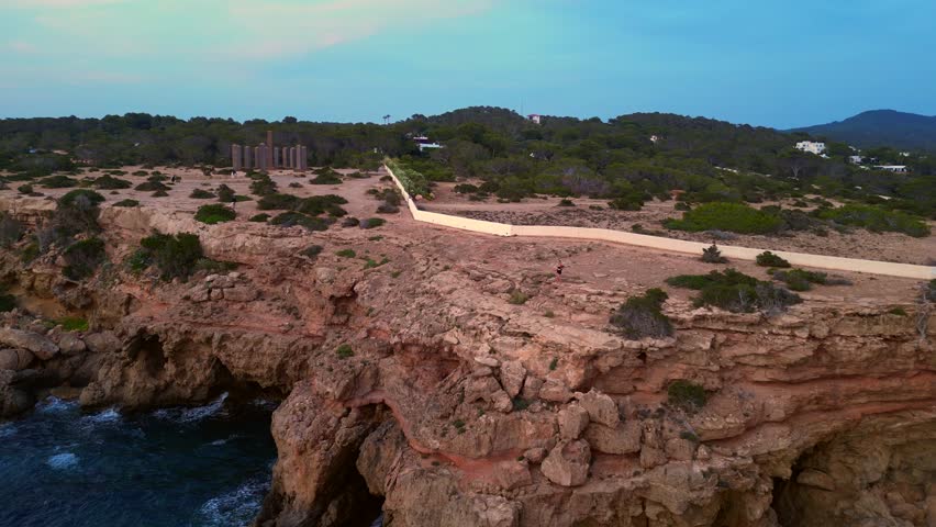 dancing Woman expressing freedom and movement by the sea at a beautiful travel destination Cala Llentia Ibiza. Magic aerial view flight pull in drone