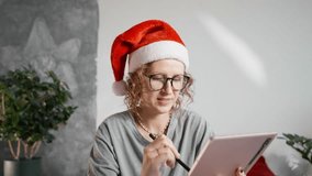 Woman in Santa hat sitting on bed with tablet and Christmas decorations around, enjoying cozy winter evening at home. Concept of holiday comfort and relaxation. - Powered by Shutterstock - Get 15% off with code: PIKWIZARD15