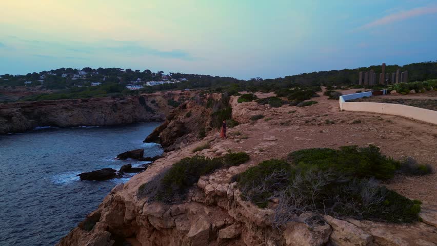 dancing Woman expressing freedom and movement by the sea at a beautiful travel destination Cala Llentia Ibiza. Perfect aerial view flight fly push forward drone