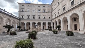 Slow pan across the courtyard of Monte Cassino Abbey in Italy, showing stone arches, historic walls, and a central fountain under soft daylight. - Powered by Shutterstock - Get 15% off with code: PIKWIZARD15