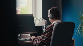 Back view of teenage black boy in wireless headphones checking coding script on computer while programming at home desk - Powered by Shutterstock - Get 15% off with code: PIKWIZARD15
