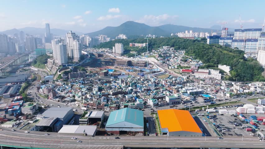 4K drone footage showing the cityscape of Uam-dong in Busan, South Korea, including Donghang Catholic Church and surrounding buildings under bright daylight.