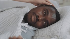 Sick black man laying in bed when feeling fever, woman caring about him, closeup. Face of exhausted and depressed male person, seasonal viral disease, epidemic of respiratory viruses in autumn - Powered by Shutterstock - Get 15% off with code: PIKWIZARD15