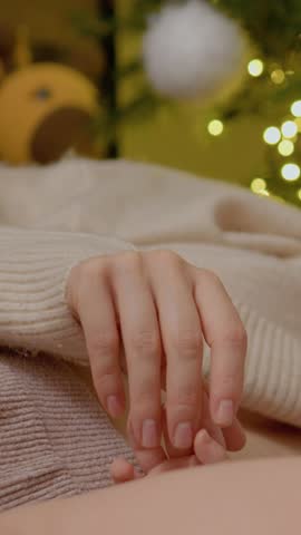 Vertical Screen: A young mother lovingly breastfeeds her baby while lying on a cozy blanket next to a beautifully decorated Christmas tree adorned with lights and ornaments.