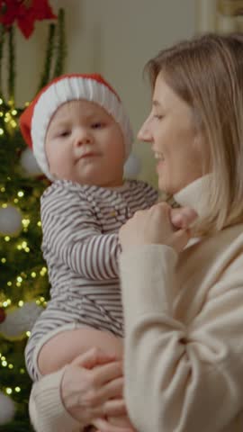 Vertical Screen: A young mother shares a joyful moment with her little boy as they dance next to a beautifully decorated Christmas tree, surrounded by holiday cheer and warmth.