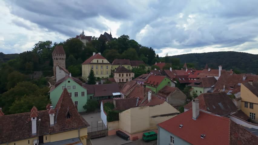 Panoramic view of the old town and surrounding hills of Sighișoara from the Clock Tower under a cloudy sky in Romania.