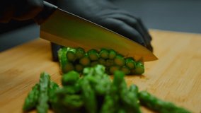 Chef's gloved hand precisely slicing fresh green asparagus spears into small pieces on a bamboo cutting board, preparing healthy ingredients for a nutritious meal - Powered by Shutterstock - Get 15% off with code: PIKWIZARD15