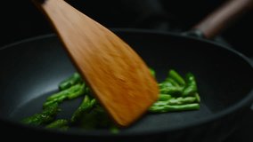 Fresh green asparagus being stir-fried in a hot cast-iron pan with a wooden spatula, showcasing healthy vegan cooking, fresh produce and simple home kitchen meal preparation - Powered by Shutterstock - Get 15% off with code: PIKWIZARD15