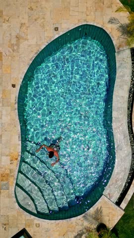 Aerial view of a single person in the vivid blue pool with steps, surrounded by light tile, Sam Roi Yot, Prachuap Khiri Khan, Thailand.