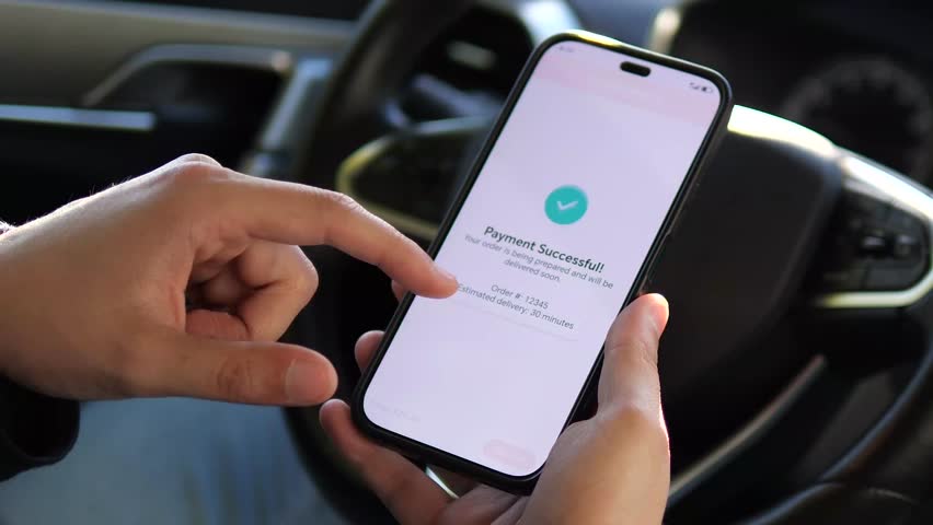 A successful digital transaction conclusion is captured in this shot of hands holding a smartphone displaying a payment confirmation message in a vehicle. This universal positive outcome scene works