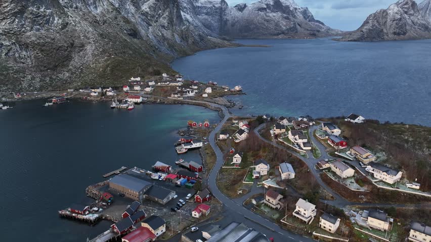 Aerial view of Reine, a small village with striking red and white buildings nestled beside a fjord and jagged, snow-capped peaks, Reine, Norway.