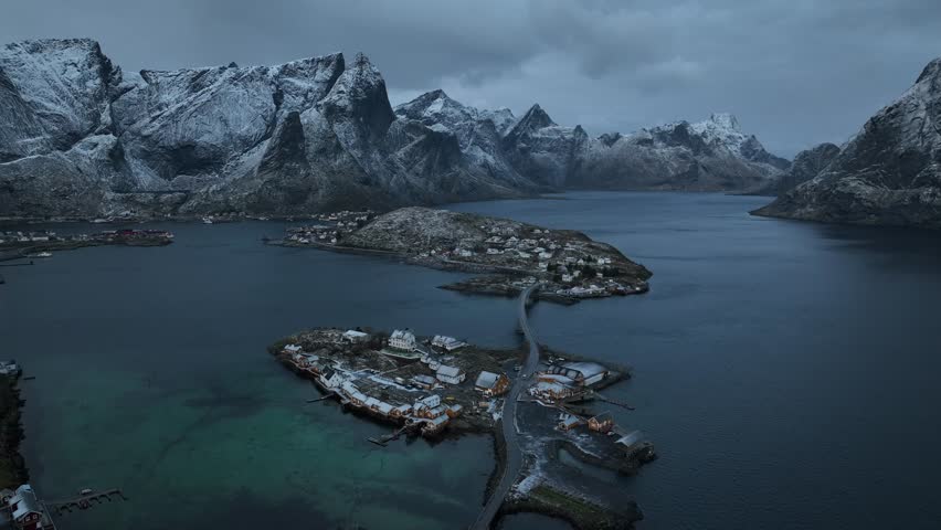 Aerial view of Reine and Hamnoy, where small islands are connected by bridges amidst dark waters against snow-capped mountains, Reine, Norway.