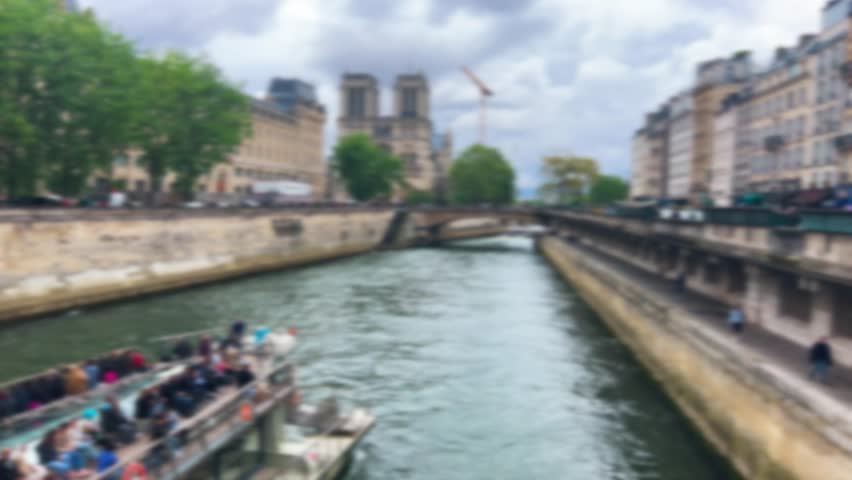 A double-deck ferry carrying tourists sails down the Seine River past the Ile de la Cite towards Notre Dame Cathedral on a cloudy spring day. Paris, France. Out of focus.