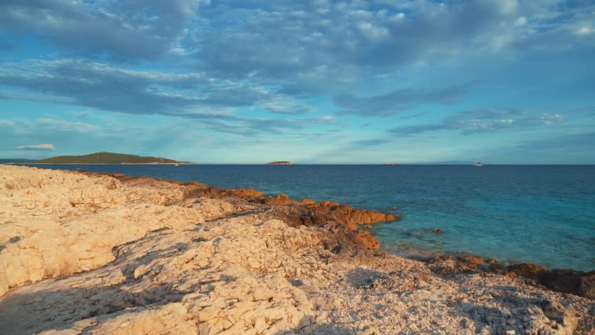 Croatia seaside beach landscape with calm waves, clear ocean water and sailboats under the evening sky
