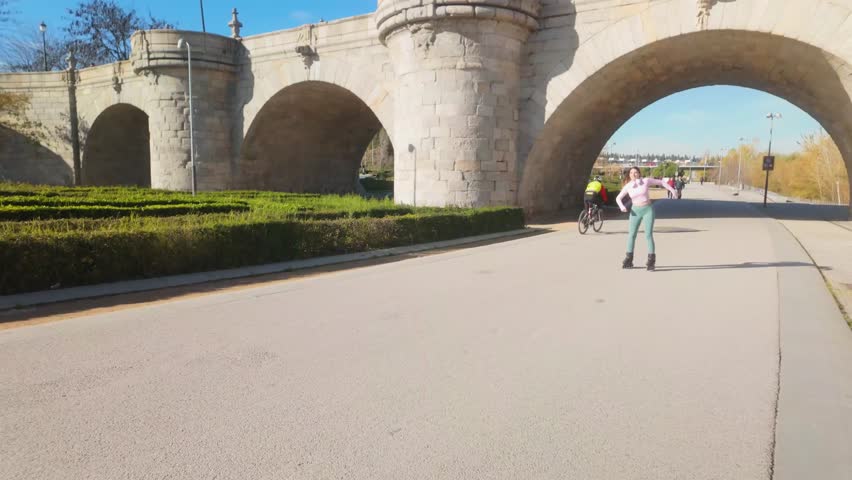 Young athletic woman roller skating on an urban path, smiling as she approaches the camera