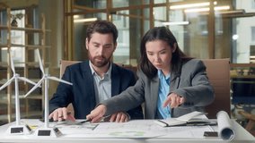 Japanese businesswoman inspector Caucasian businessman speak wind turbine model eco implementation renewable project document blueprint electricity engineering indoors office multinational meeting - Powered by Shutterstock - Get 15% off with code: PIKWIZARD15