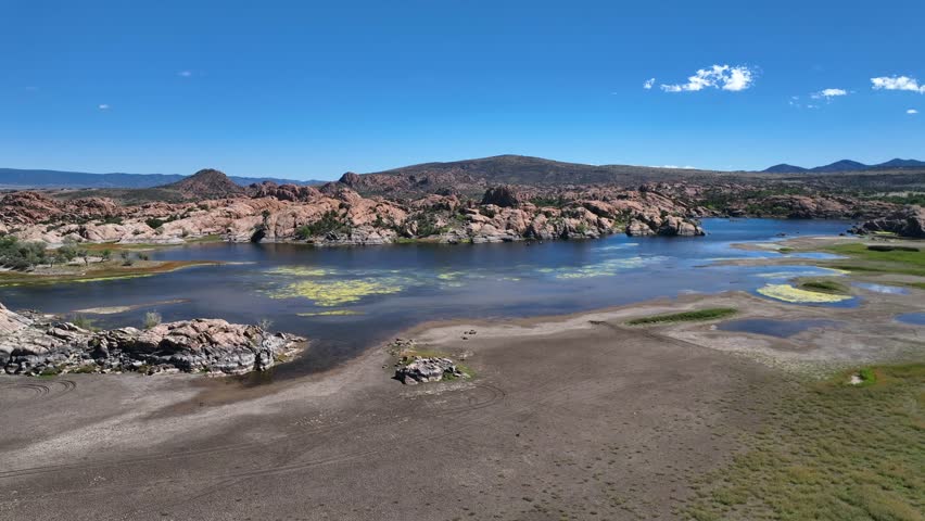 Aerial view of willow creek reservoir, reflecting the clear blue sky, contrasts with the rugged, rocky terrain and the green algae, willow creek reservoir, Arizona, United States.