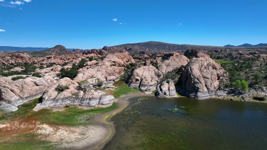 Aerial view of the tranquil Willow Creek Reservoir surrounded by rugged granite boulders contrasting with the clear blue sky above, Willow Creek, Arizona, United States.