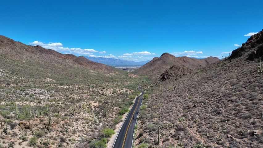 Aerial view of the winding Gates Pass Road cutting through the arid desert landscape under a bright blue sky, Gates Pass Scenic Lookout, Arizona, United States.