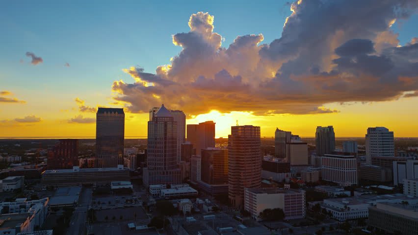 The glowing Tampa skyline during golden sunset with warm clouds, aerial tracking to the left, establishing shot