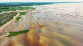 Maine shoreline at low tide reveals natural tidal flats with sand ridges, shallow pools of water reflecting the sky, and scattered dunes rising gently along the open coastline. - Powered by Shutterstock - Get 15% off with code: PIKWIZARD15