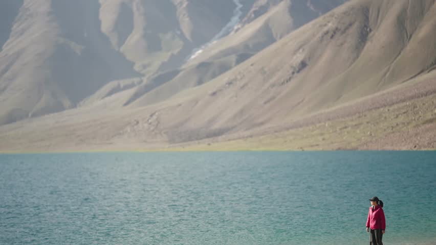 Minimal aesthetic shot of woman in red jacket at Chandratal Lake, serene landscape and reflective mountain water.